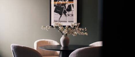 Una habitación con una mesa redonda, dos sillas, un florero con flores y un cuadro en la pared.