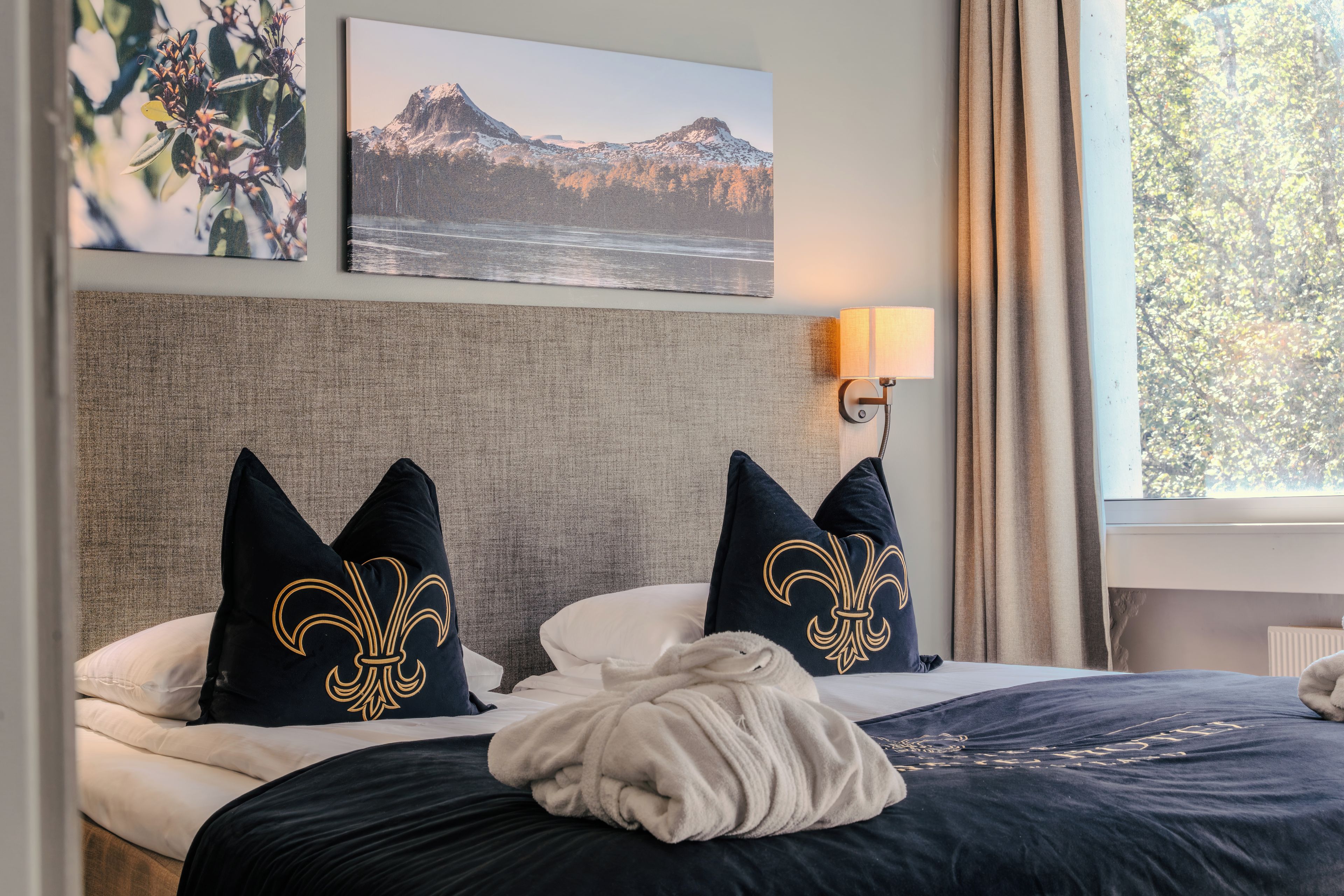 Une chambre d’hôtel avec un lit, une tête de lit, une lampe fixée au mur et une fenêtre avec des rideaux.