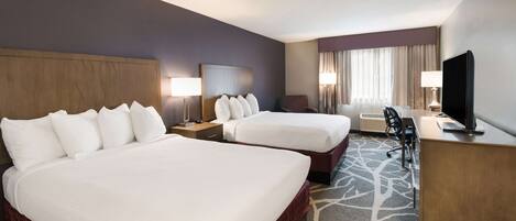 A hotel room with two beds, a desk, a TV, and a window with curtains.