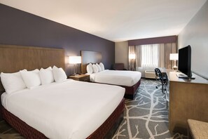 Habitación de hotel con dos camas, un escritorio, un televisor y una ventana con cortinas.