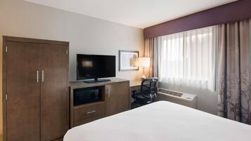 A hotel room with a bed, a TV, a desk with a lamp, a chair, and a wardrobe.