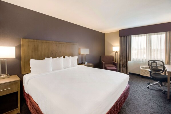 Una habitación de hotel con una cama grande, un escritorio, una silla y una ventana con cortinas.