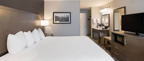 Habitación de hotel con una cama grande, un escritorio con silla, televisión y baño con espejo y lavamanos.