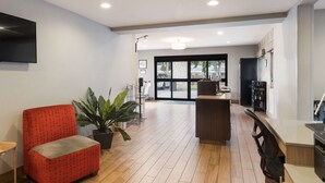 A modern lobby with a red armchair, potted plants, a reception desk, and a large window offering a view of the outside. - Best Western McMinnville Inn (McMinnville)