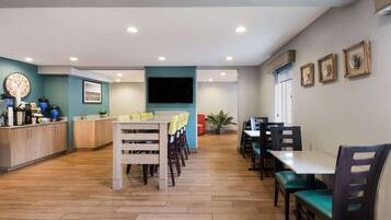 A modern dining area with wooden flooring, a central table with chairs, and a flat-screen TV mounted on the wall.