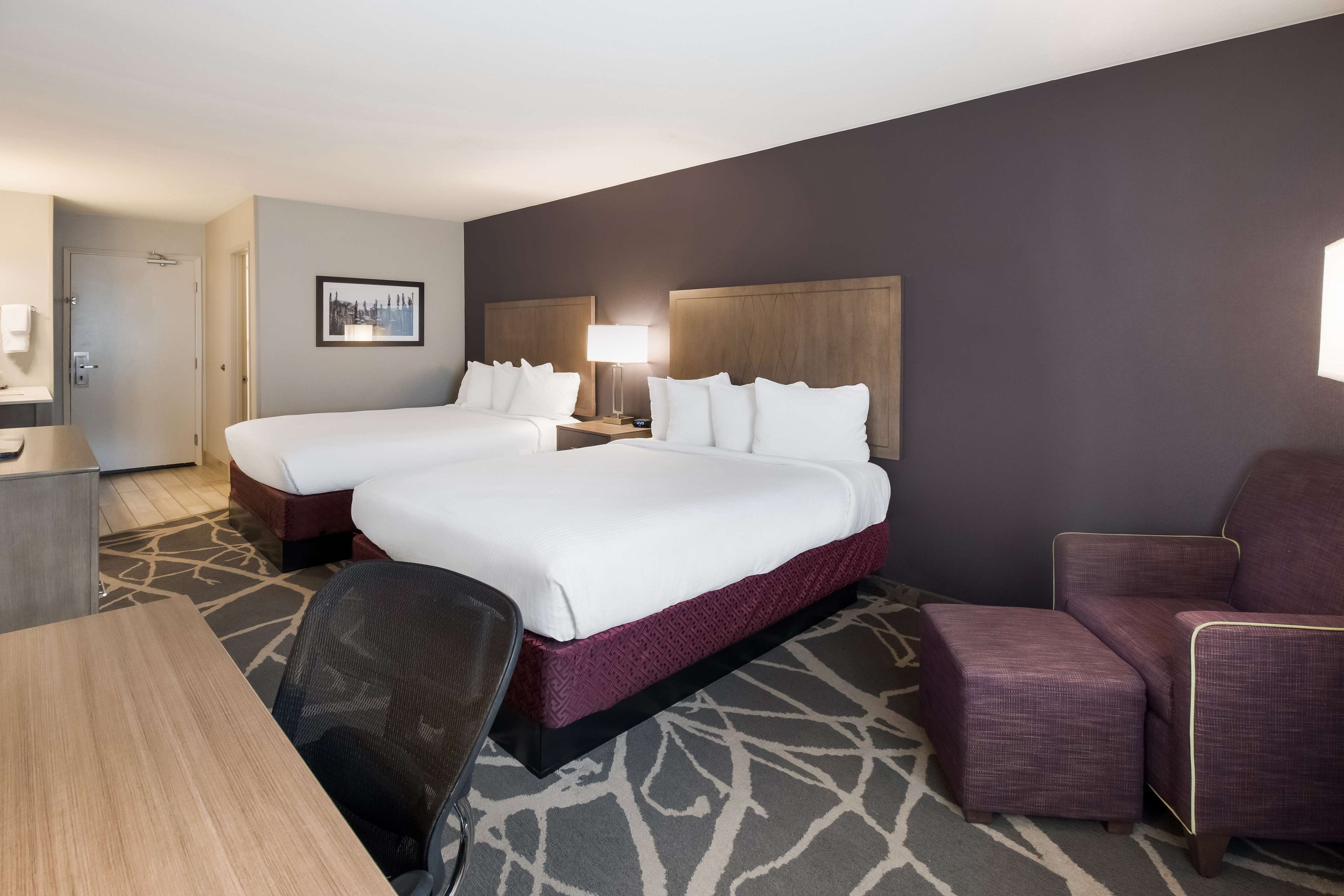 A hotel room with two beds, a desk, a chair, and a couch.