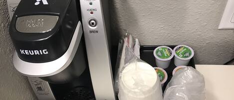 A Keurig coffee machine with a cup of coffee, a milk jug, and reusable cups on a tray.