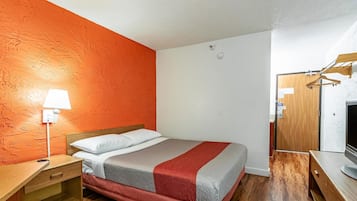 Un dormitorio con cama, mesita de noche, lámpara, escritorio de madera, televisor y armario.