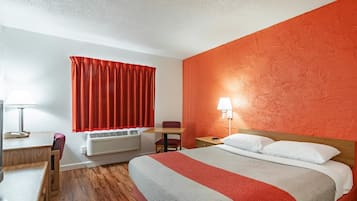 Et hotelværelse med seng, skrivebord, stol, lampe og varmeblæser.