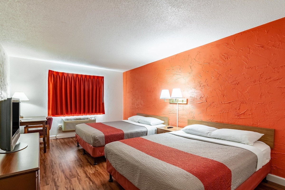 A hotel room with two beds, a desk with a chair, a TV, and a red curtain.