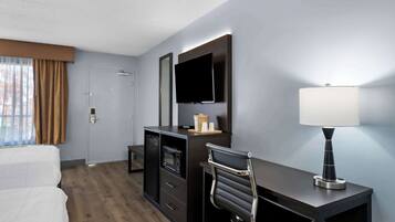 Una habitación de hotel con cama, escritorio, silla, televisor, lámpara y minibar.