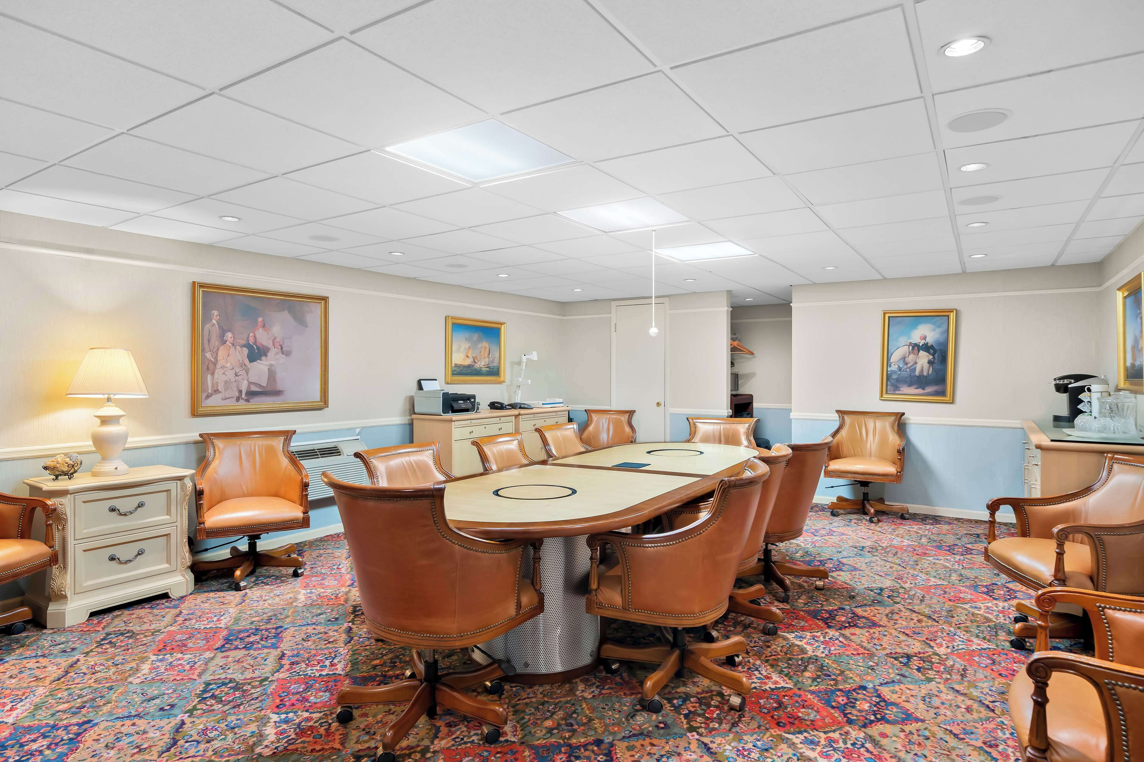 Uma sala de conferências com uma mesa oval grande, cadeiras de couro, um tapete estampado e obras de arte nas paredes.