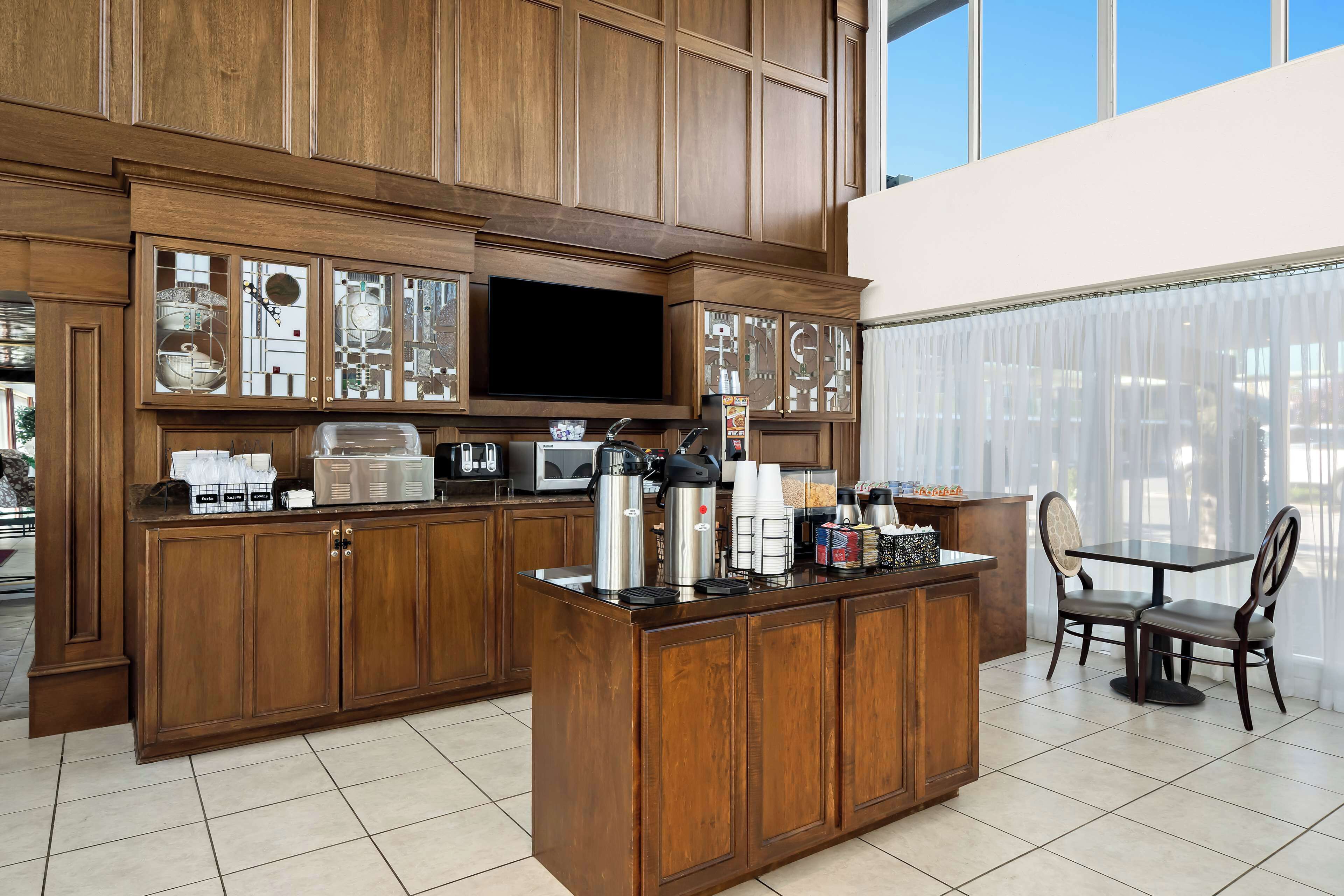 A spacious kitchen with wooden cabinetry, a large island with coffee-making equipment, and a dining area with two chairs.