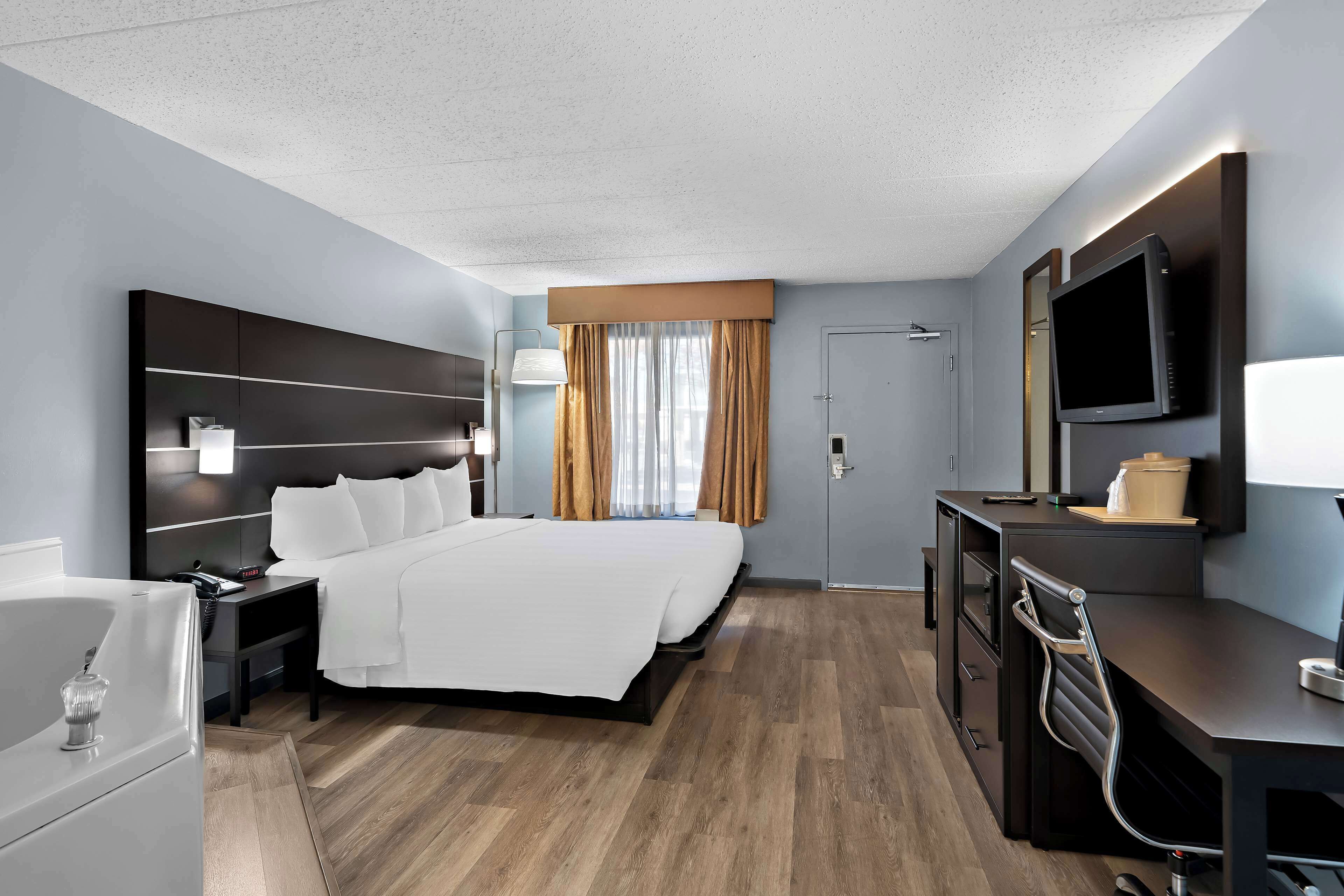 Una habitación de hotel moderna con una cama grande, un escritorio con silla, televisión y un baño con bañera y lavamanos.