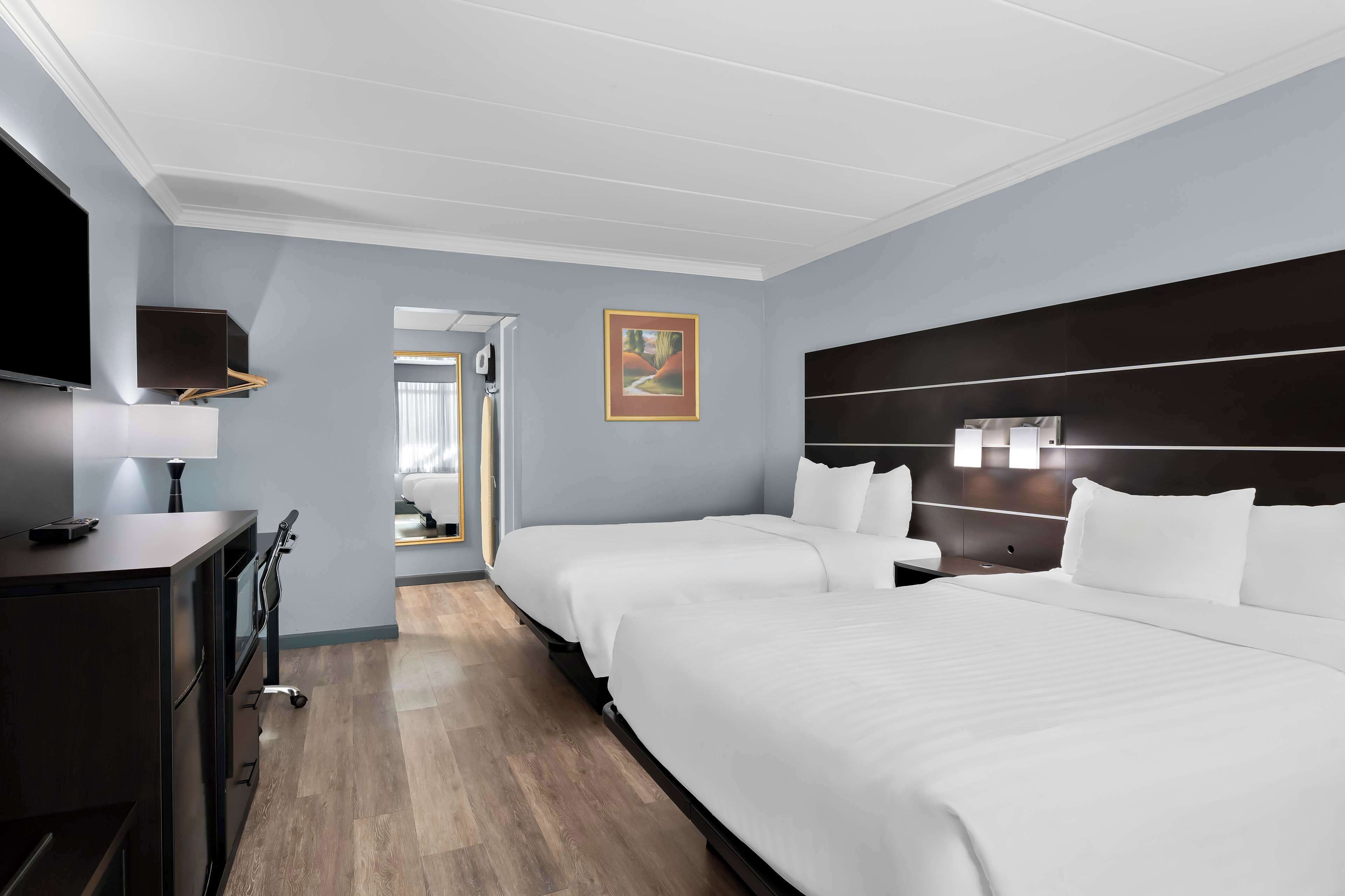 A hotel room with two beds, a desk with a lamp, a TV, and a painting on the wall.