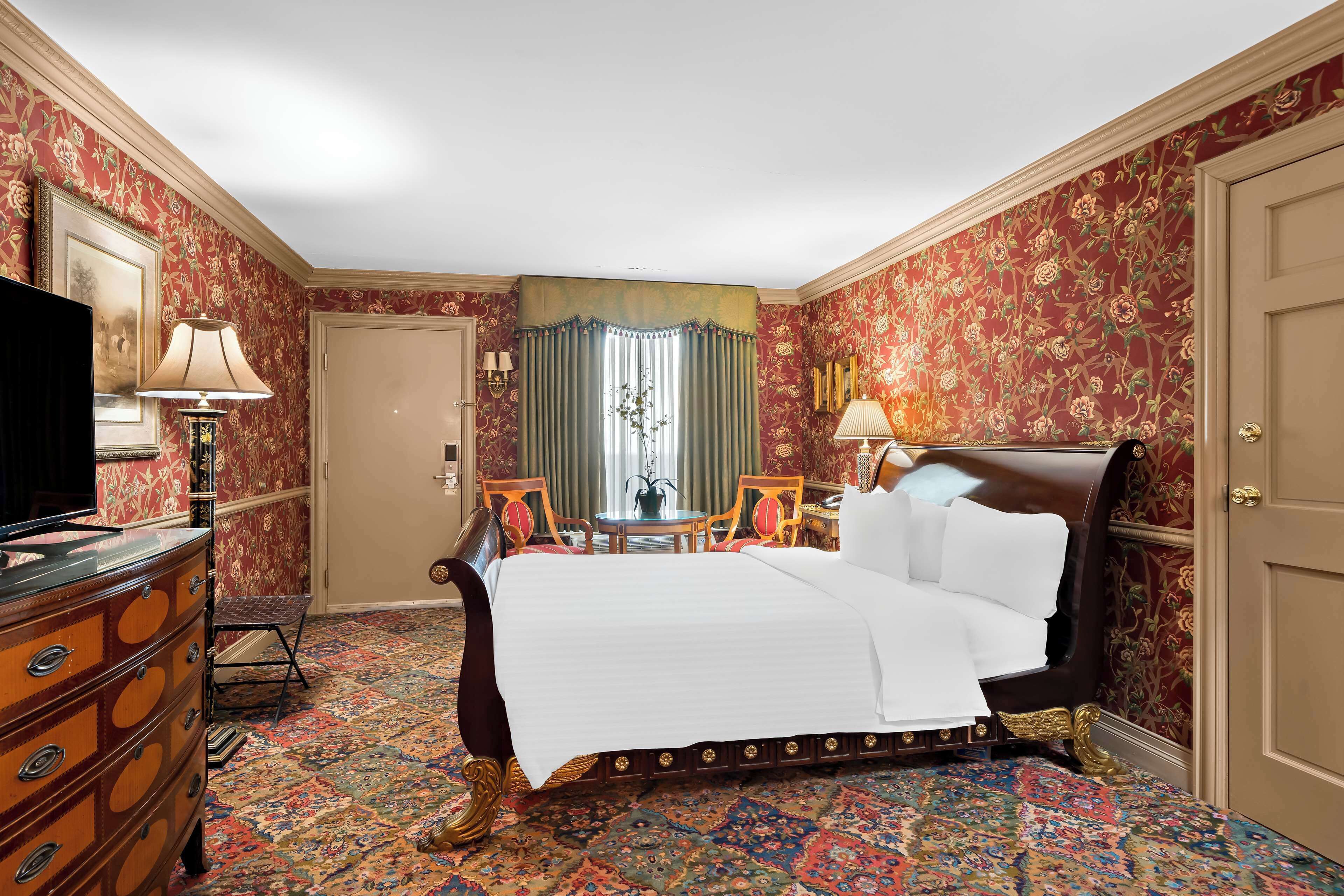 A hotel room with a large bed, a dresser, a television, and a small table with chairs.