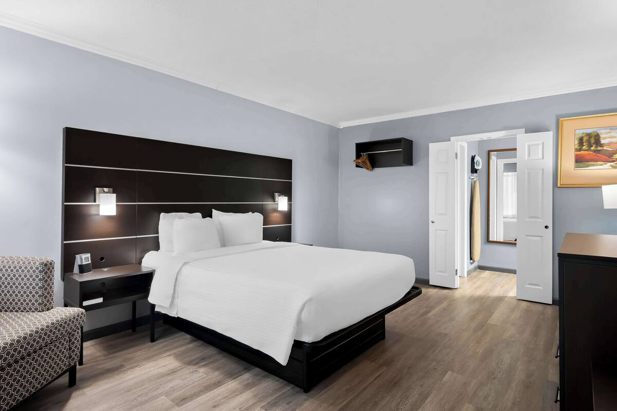 Une chambre d’hôtel moderne avec un grand lit, des tables de chevet, une chaise, une armoire et un tableau au mur.