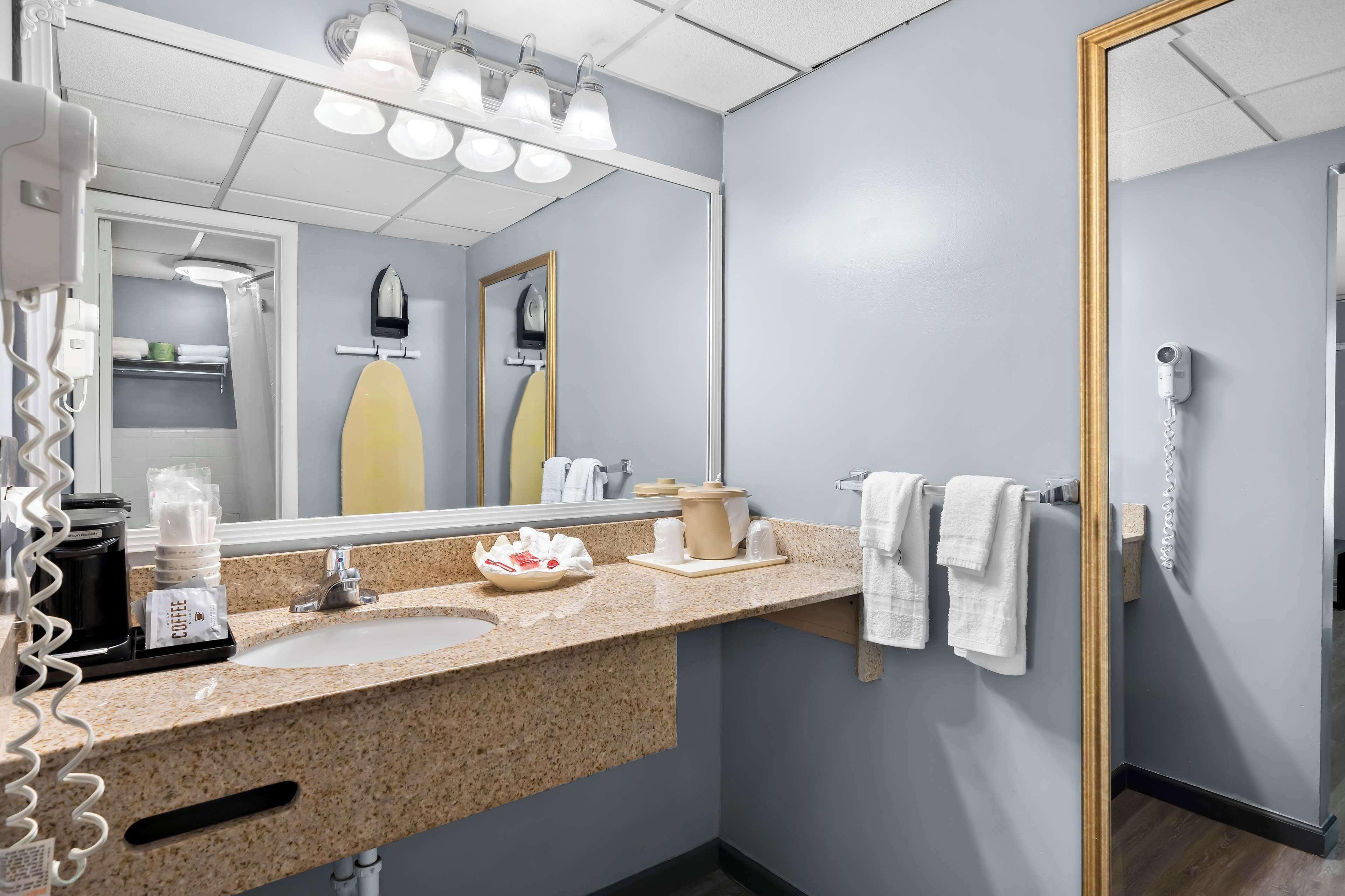 A hotel bathroom with a sink, mirror, towel rack, and a shower area.