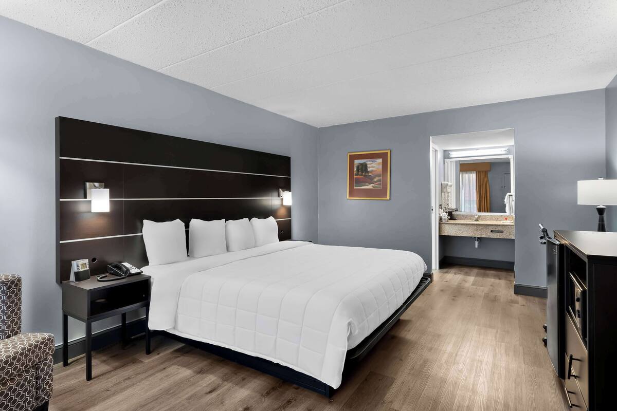 Une chambre d’hôtel moderne avec un grand lit, des tables de chevet, une petite table, un bureau et un miroir.