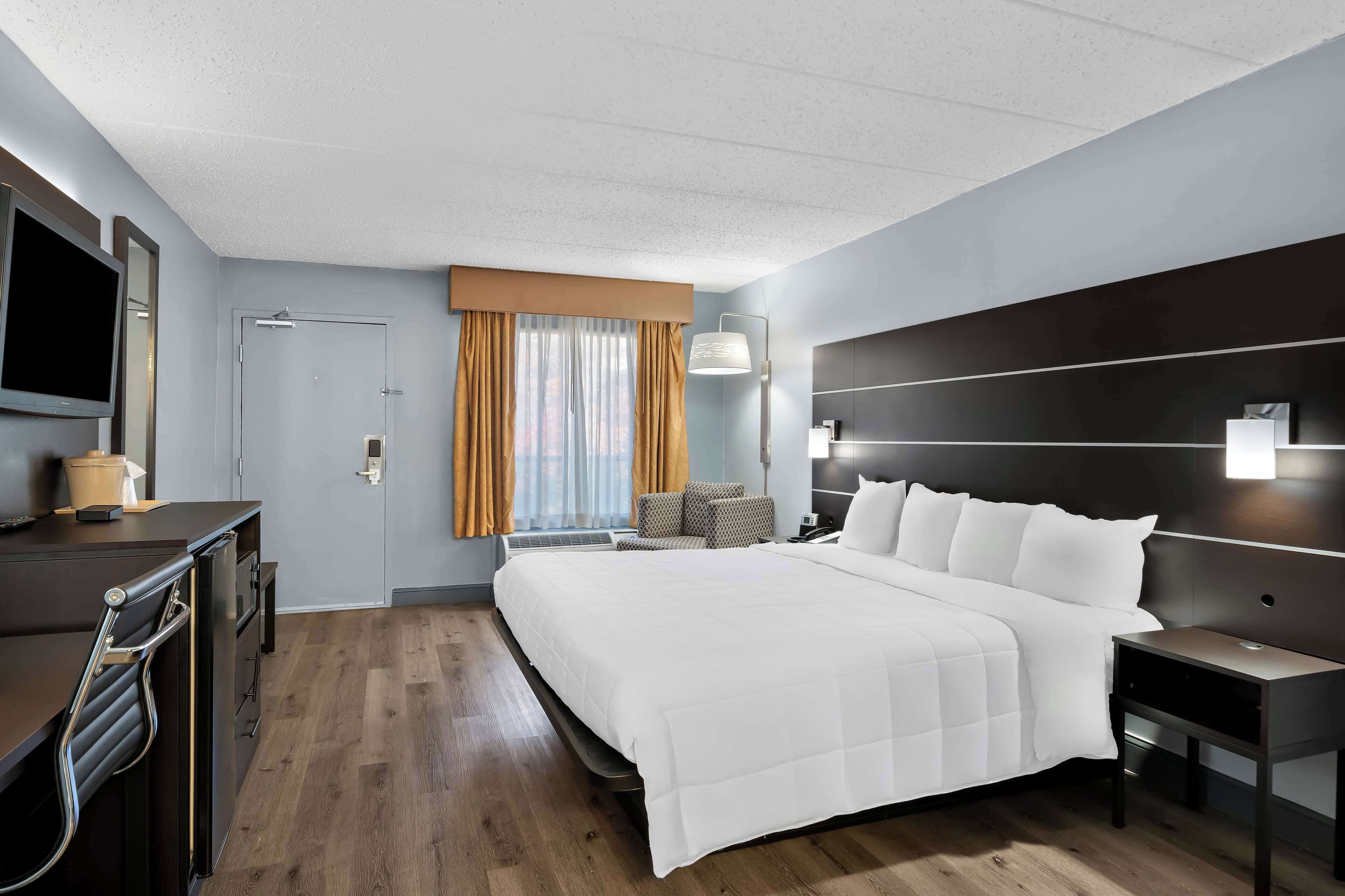 Una habitación de hotel moderna con una cama grande, un escritorio con una silla, un televisor y una ventana con cortinas.
