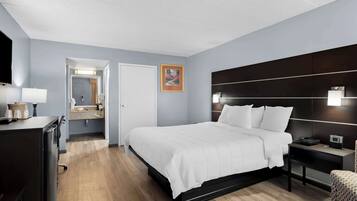 A modern hotel room with a large bed, a bedside table with a lamp, a TV, and a bathroom visible through an open door.
