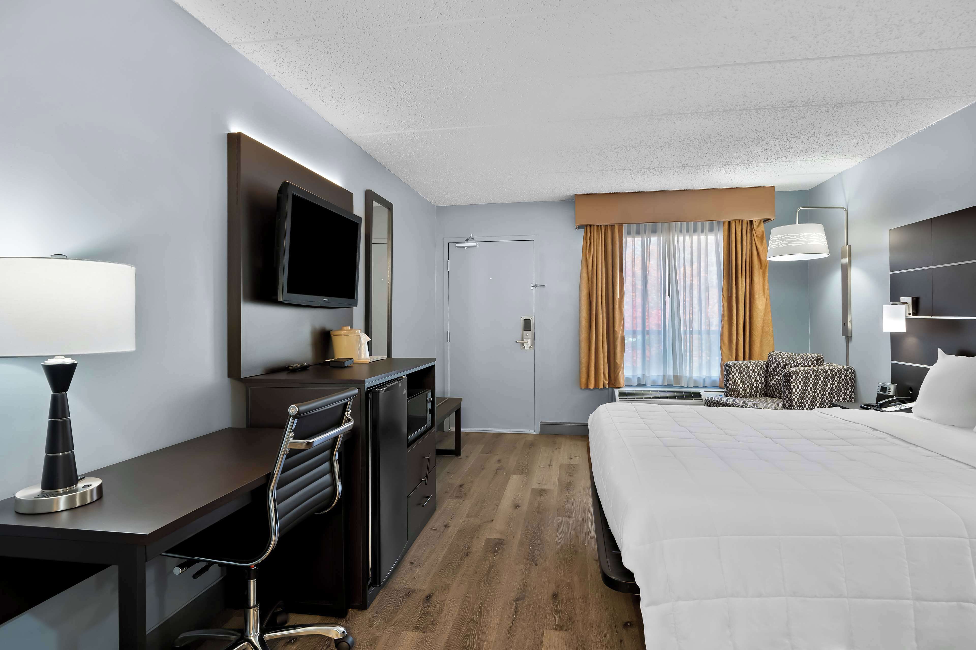 A hotel room with a bed, desk, chair, TV, and a window with curtains.