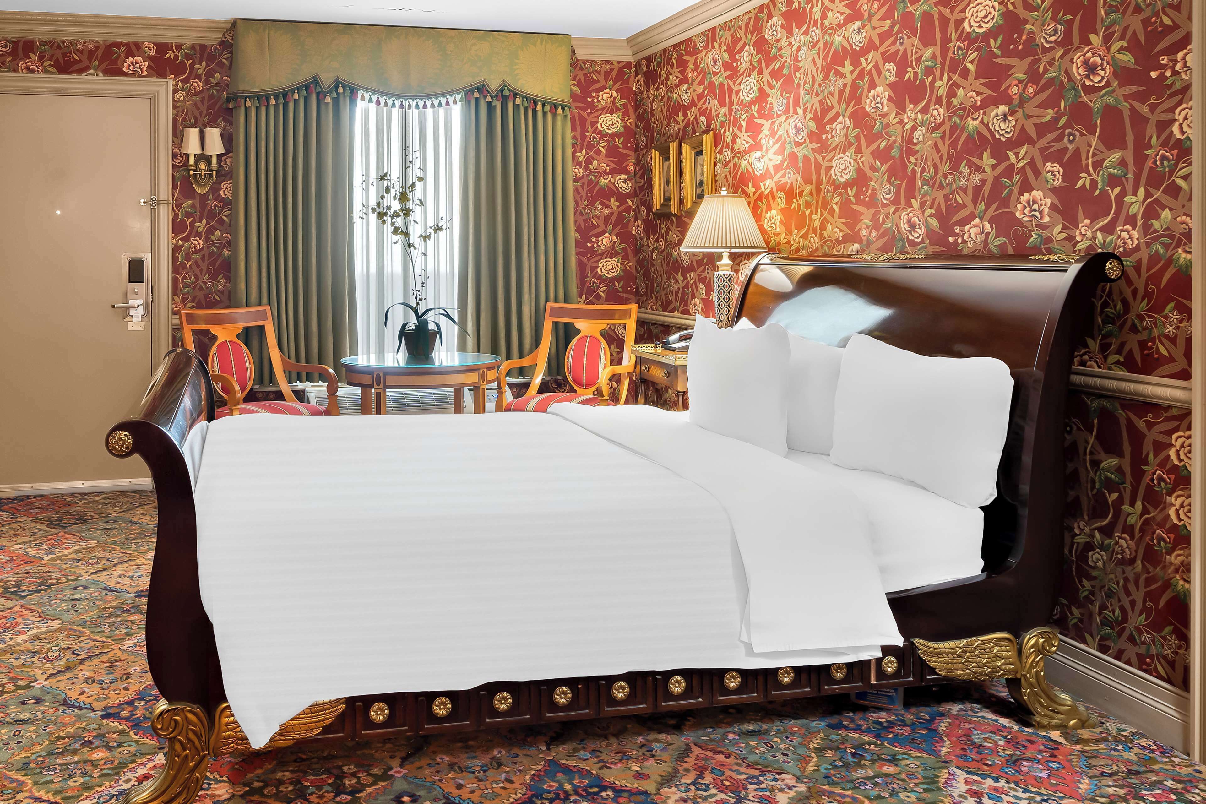 A hotel room with a large bed, a small table, two chairs, a desk, and a lamp.