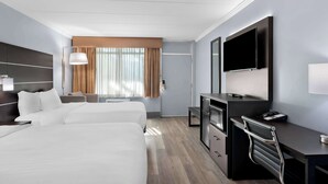 Hotelkamer met twee bedden, een bureau, een flatscreen-tv, een lamp en een raam met gordijnen.