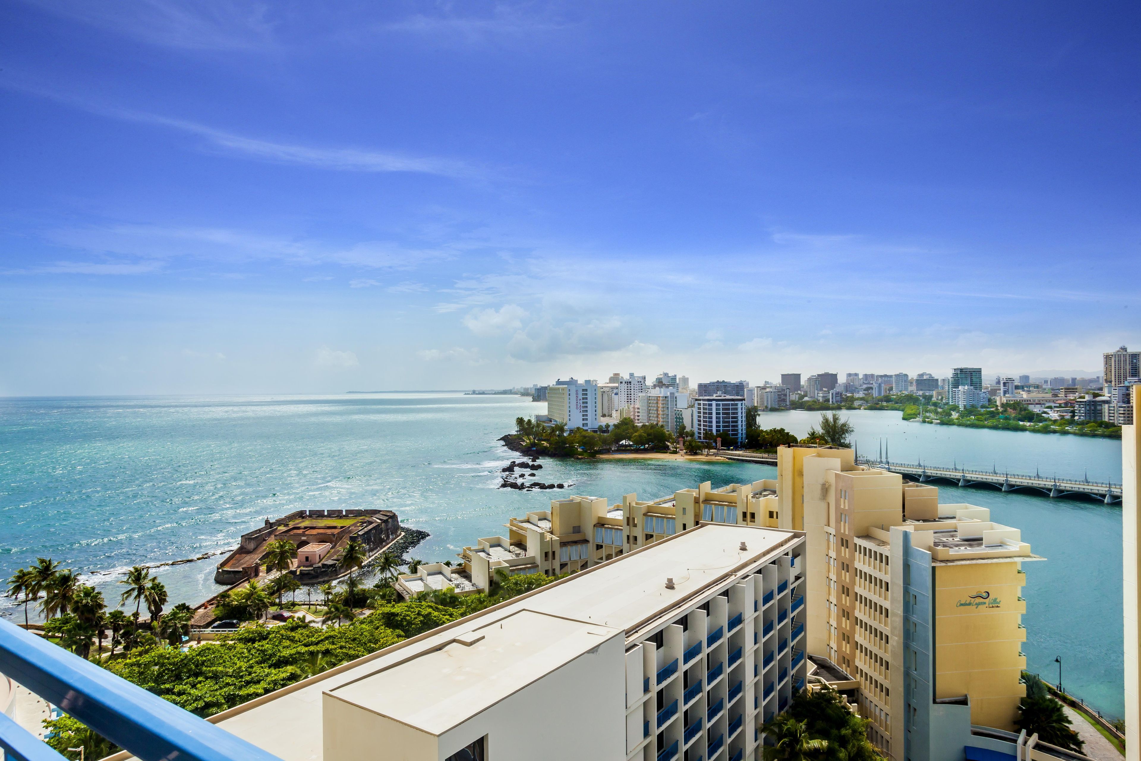 A high-rise hotel overlooking a coastal cityscape with a clear view of the ocean and a bridge.
