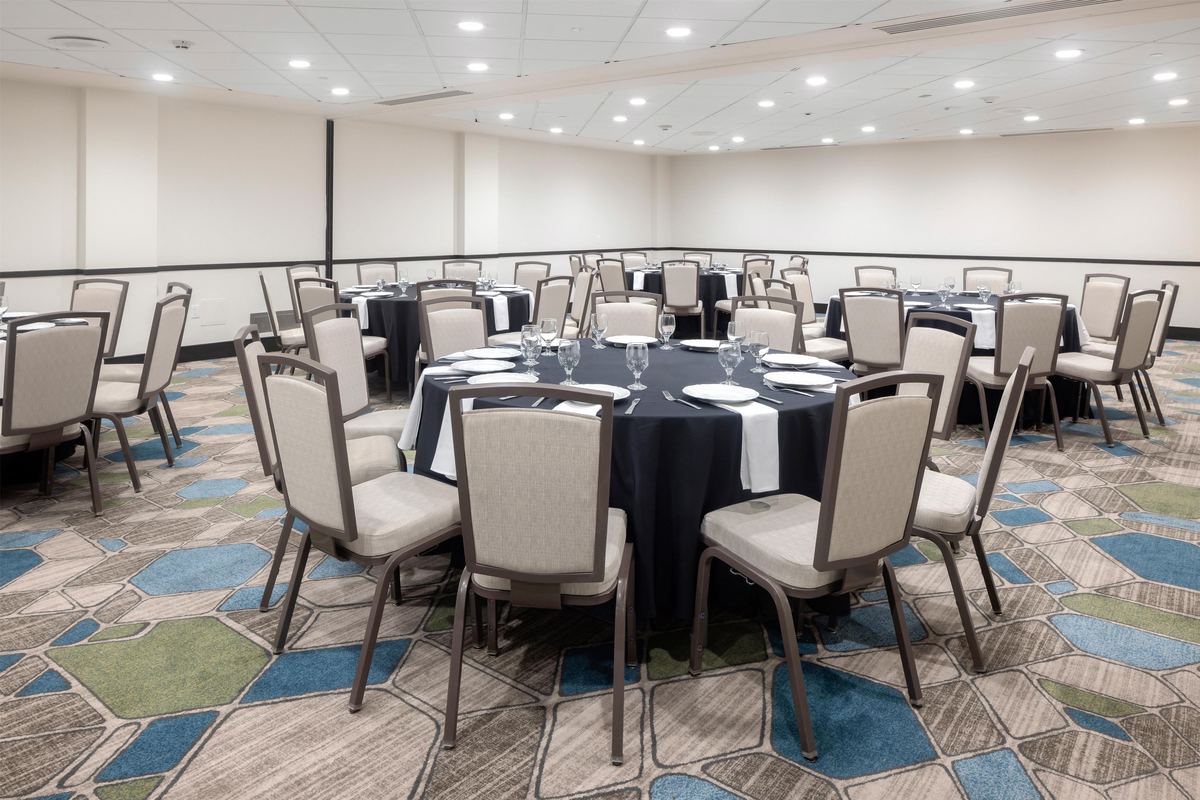Sala de conferências com mesas redondas, cadeiras e tela de projeção.
