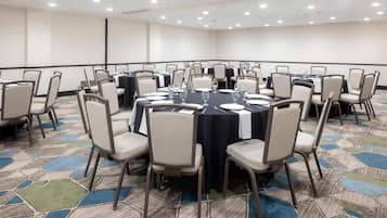 Sala de conferências com mesas redondas, cadeiras e tela de projeção.