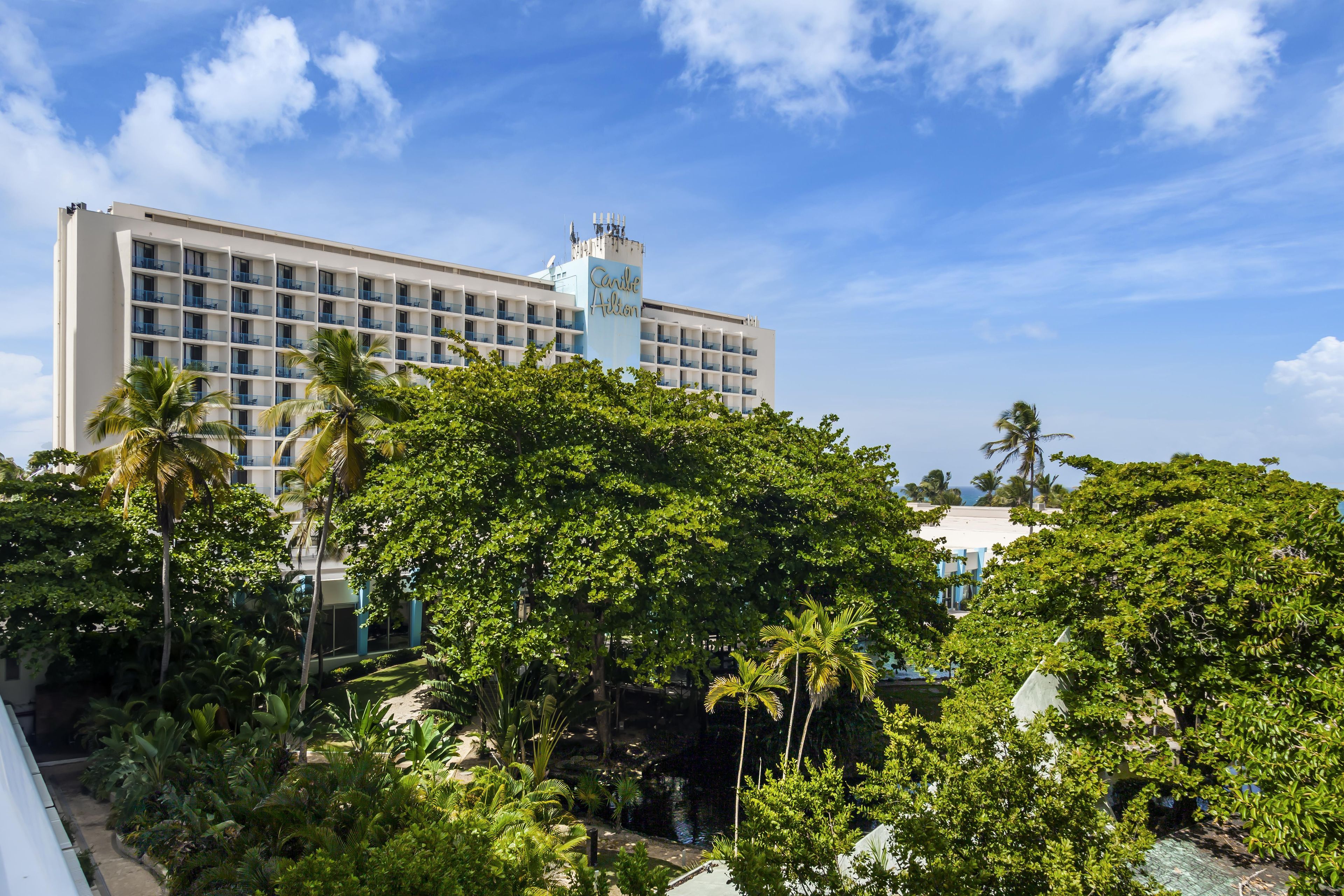 A hotel with multiple floors, a prominent tower, and lush greenery in the foreground.