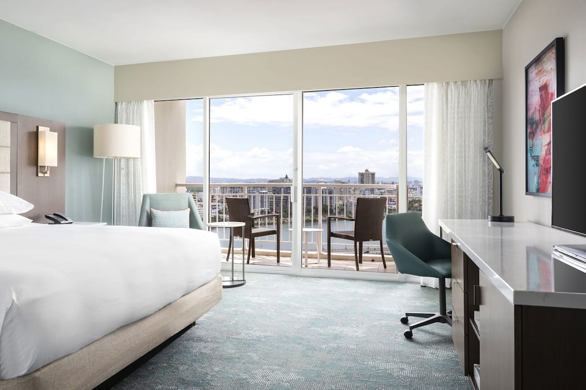 Habitación de hotel con cama, escritorio, sillas y un ventanal con vistas a la ciudad.