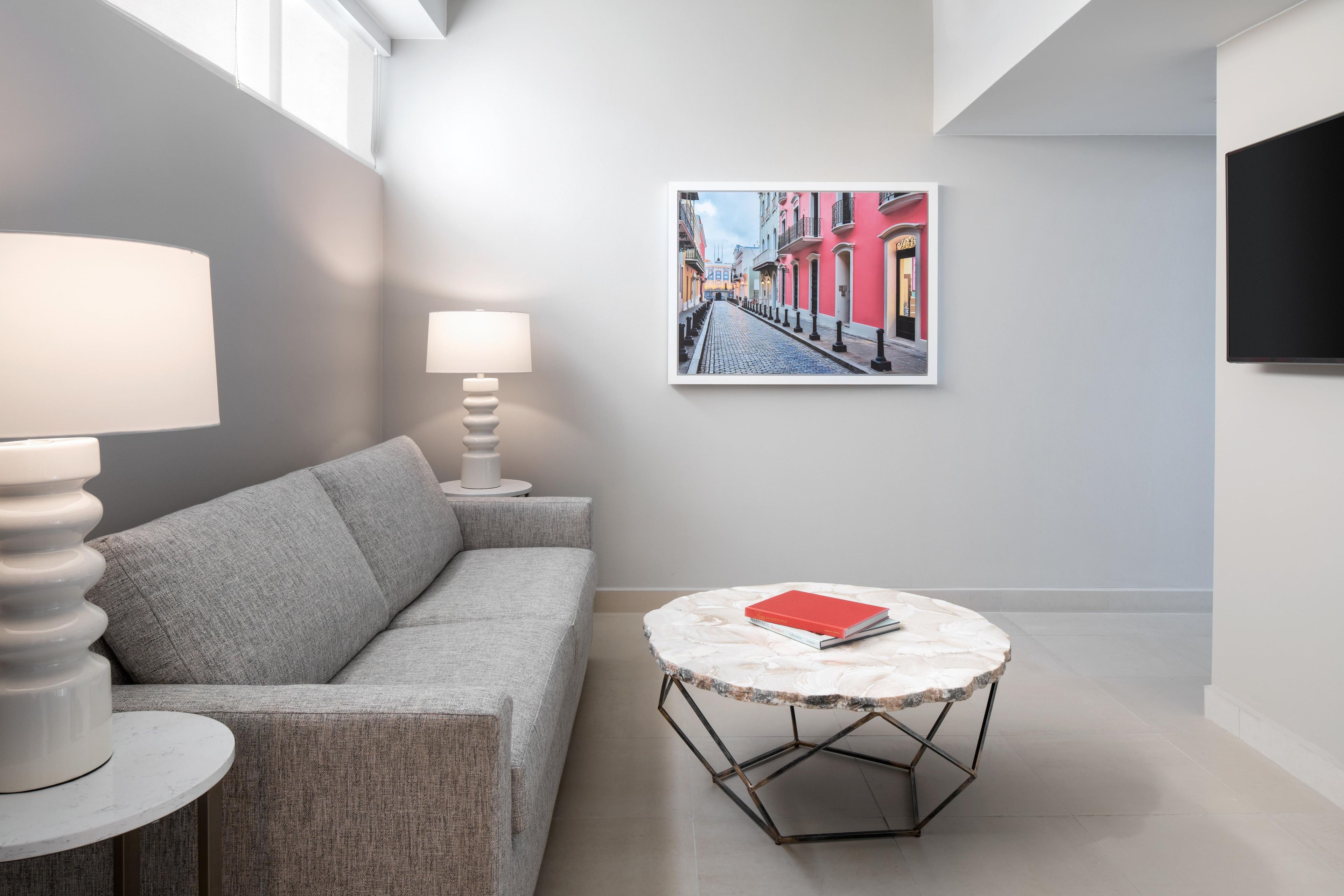Een moderne woonkamer met een grijze bank, een ronde tafel met een boek, en een gekaderd stadsgezicht aan de muur.