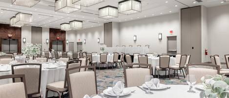 A large banquet hall with multiple round tables set for dining, equipped with chairs and table settings.