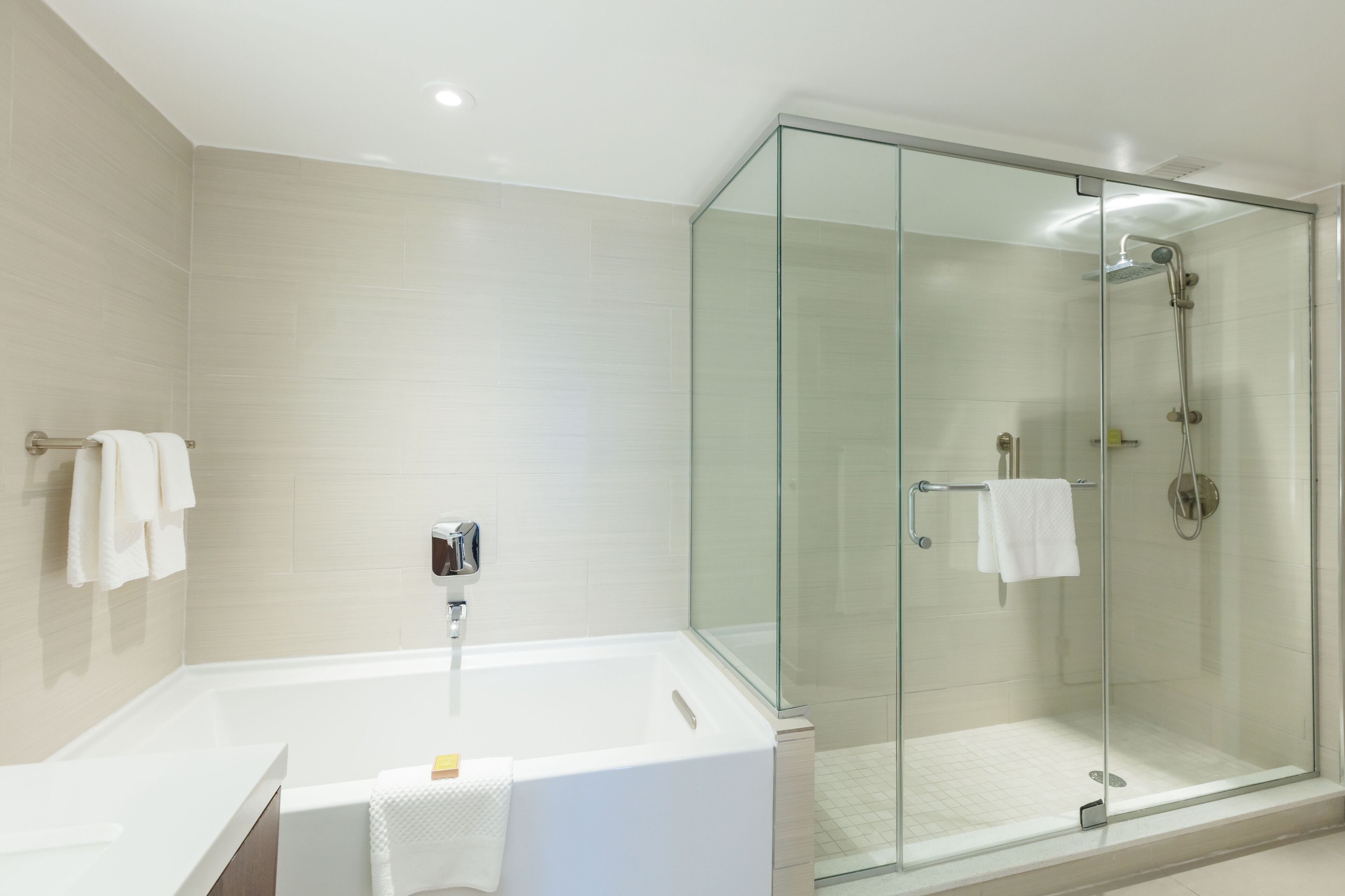 Un baño moderno con ducha acristalada, bañera blanca y lavamanos con toalla.