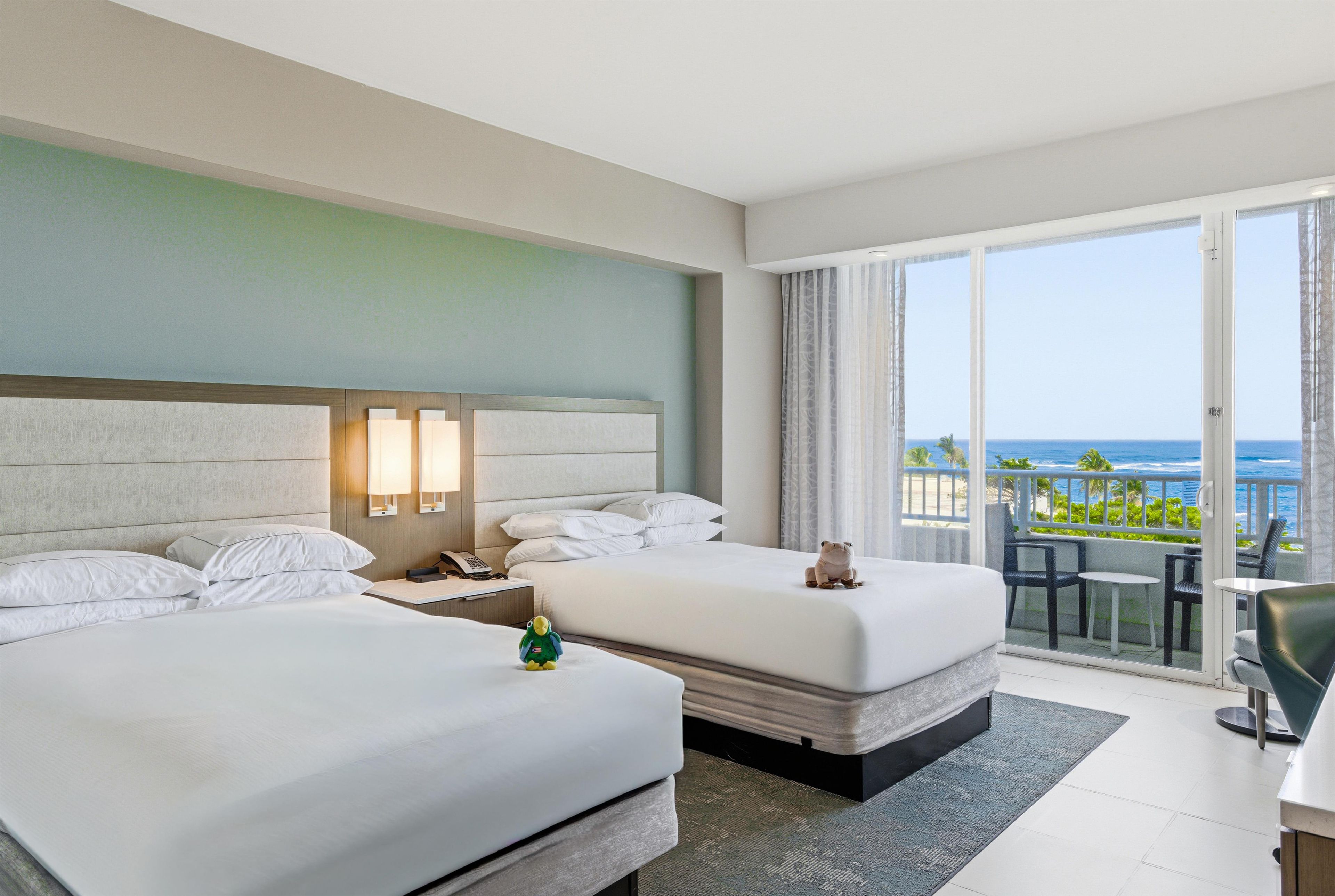Habitación de hotel con dos camas, un escritorio y un balcón con vista al océano.