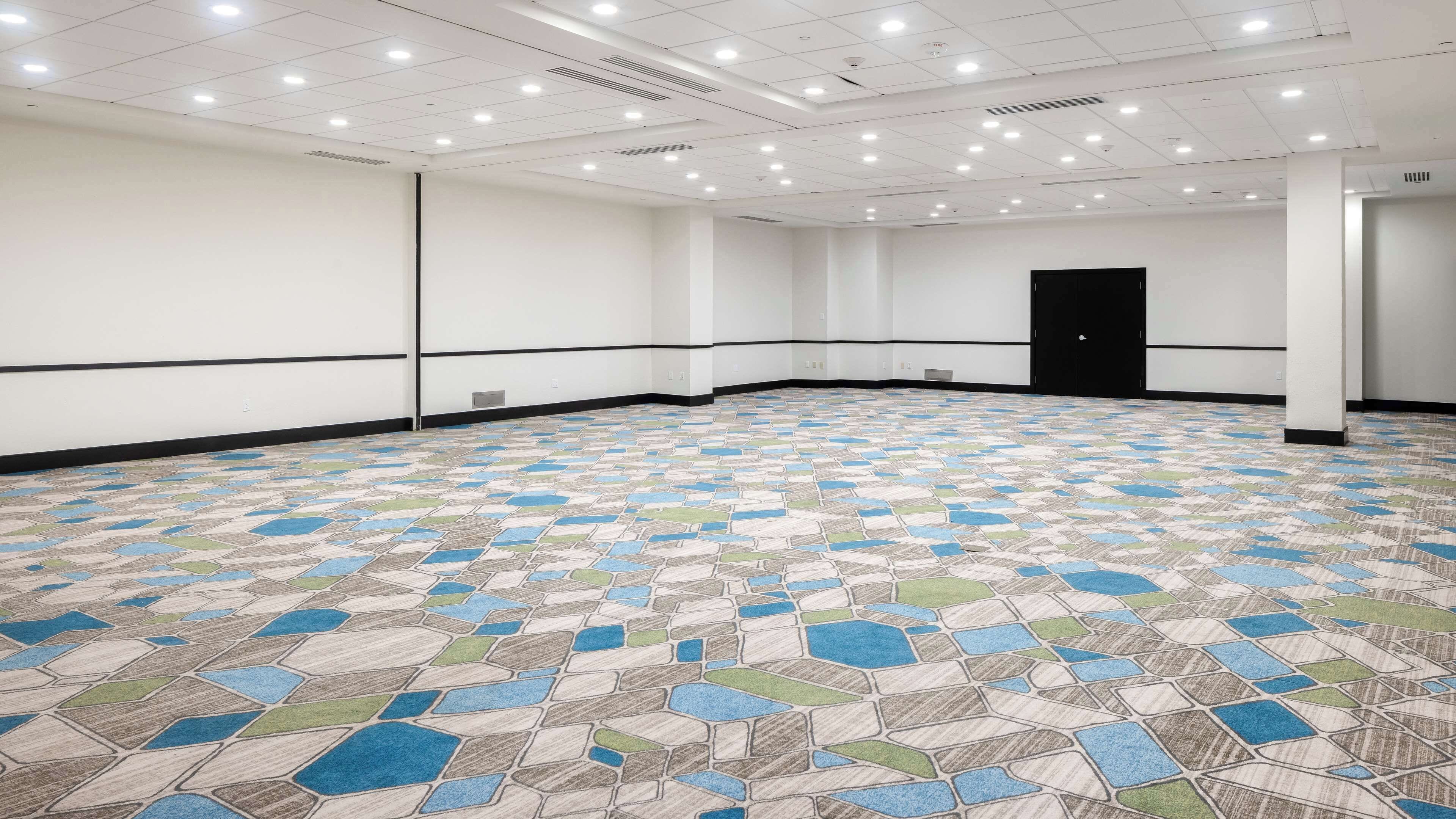 A large, empty conference room with a patterned floor, white walls, and a black door.