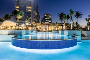 A swimming pool with a blue-tiled edge, surrounded by palm trees and modern buildings in the background. - Caribe Hilton (San Juan)