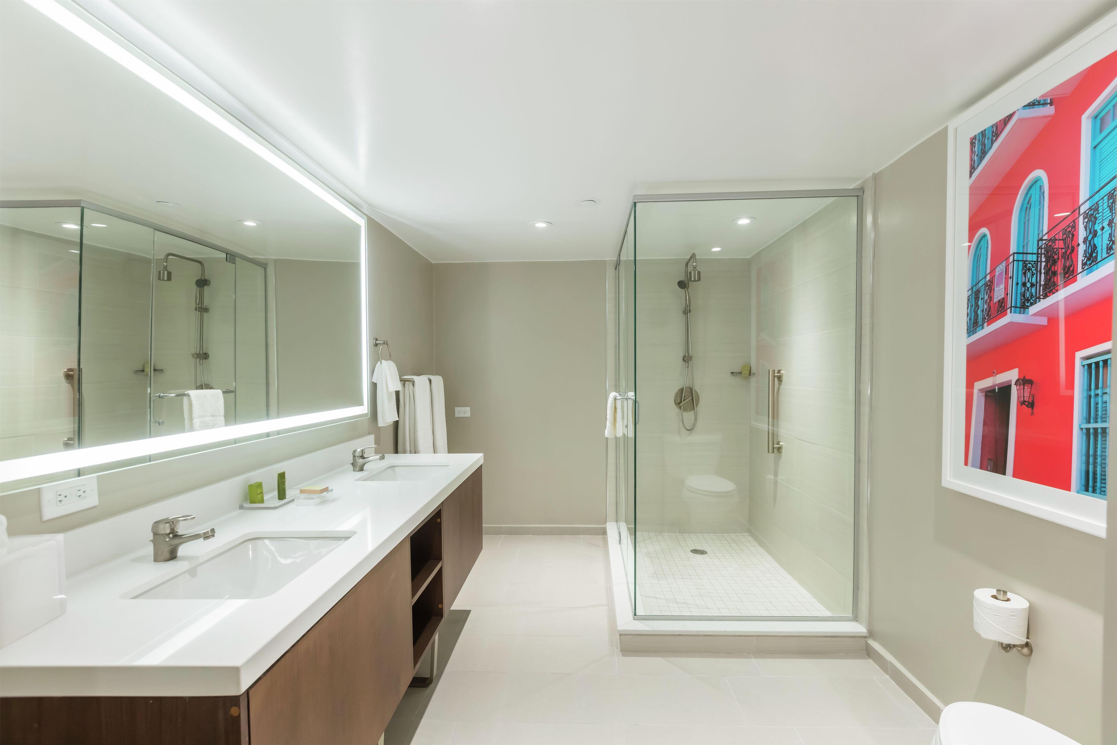 Un baño moderno con ducha envuelta en vidrio, un espejo grande y un tocador con doble lavabo.