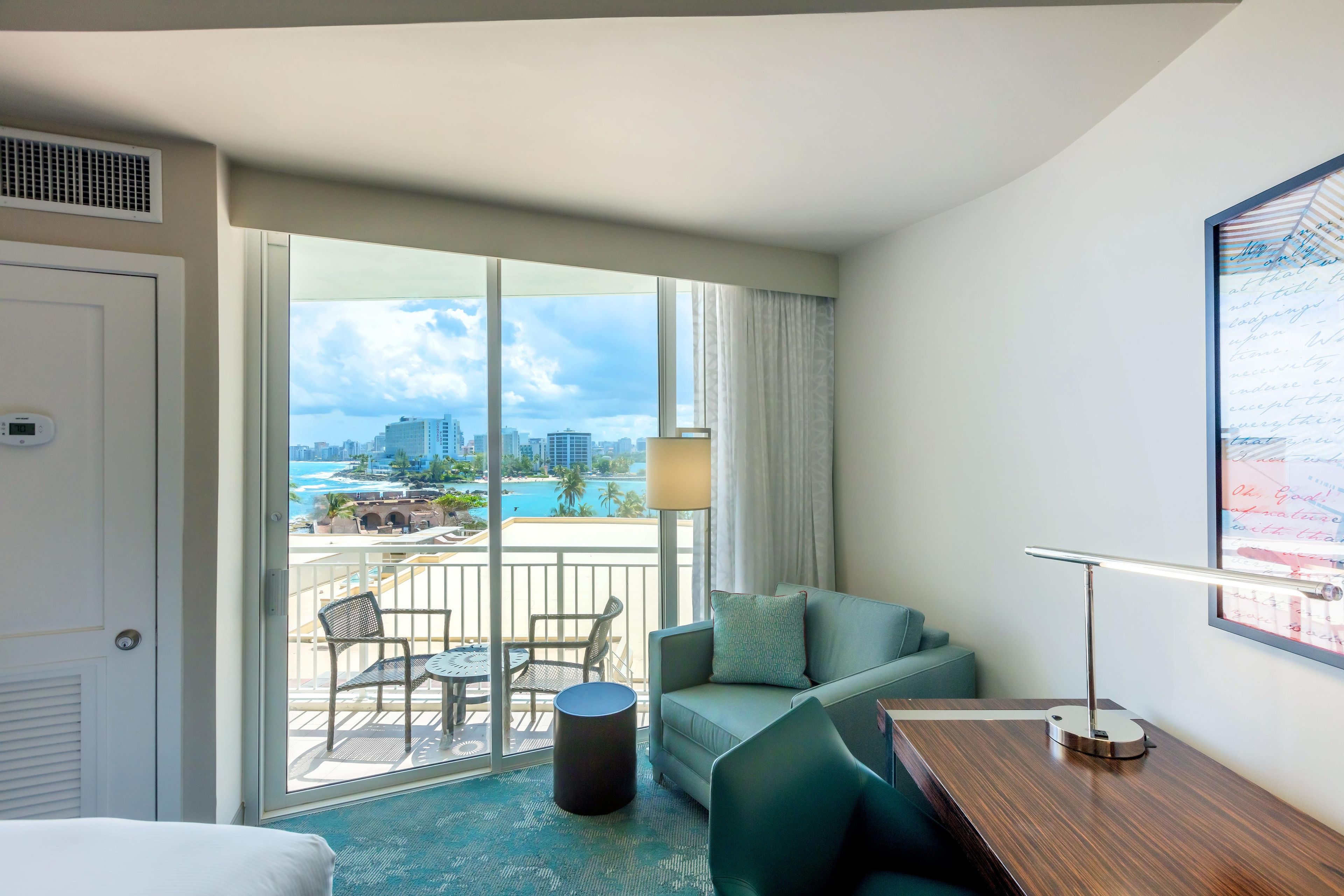 A hotel room with a balcony, a view of the city, a desk, and a bed.