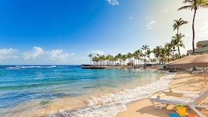 A beach with clear blue water, palm trees, and lounge chairs. - Caribe Hilton (San Juan)