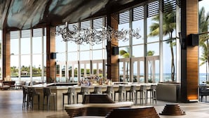 A modern bar area with a curved seating arrangement, large windows offering views of the ocean, and a decorative metal chandelier. - Caribe Hilton (San Juan)
