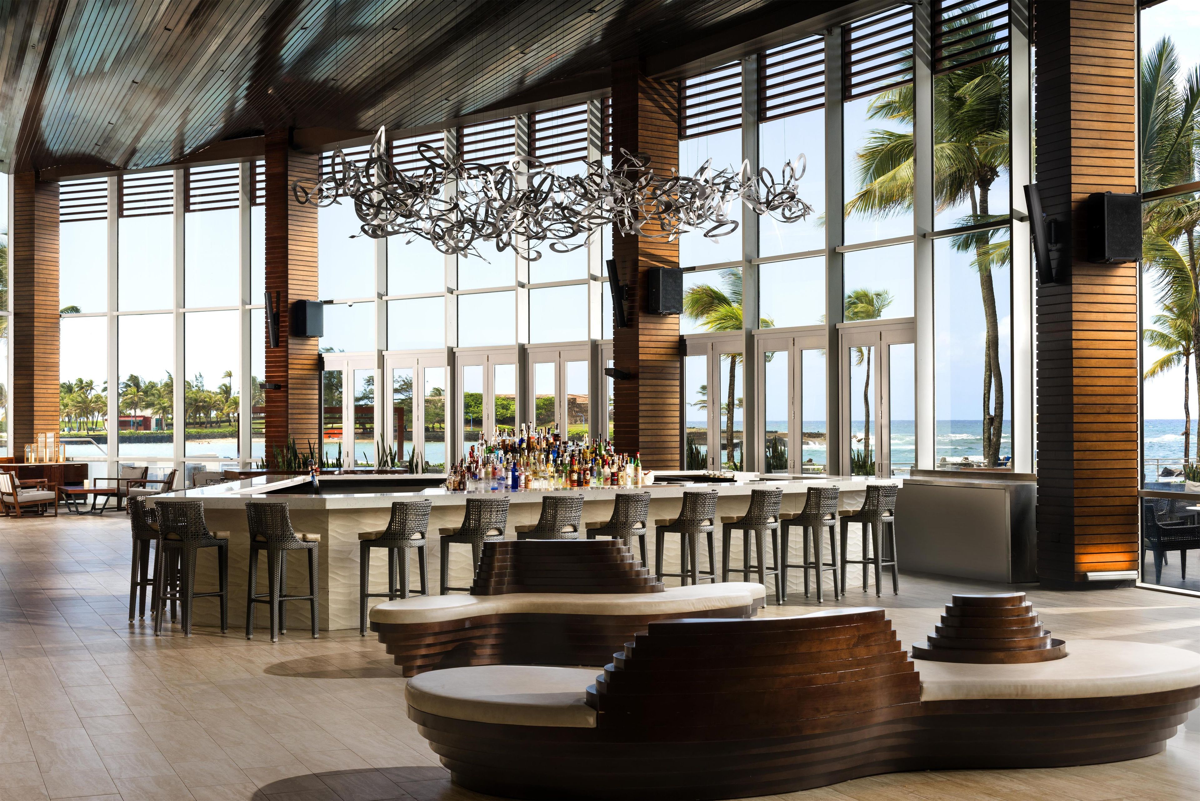 A bar area with a view of the ocean, featuring a modern design with wooden accents and a unique chandelier.
