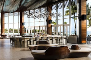 A bar area with a view of the ocean, featuring a modern design with wooden accents and a unique chandelier. - Caribe Hilton (San Juan)