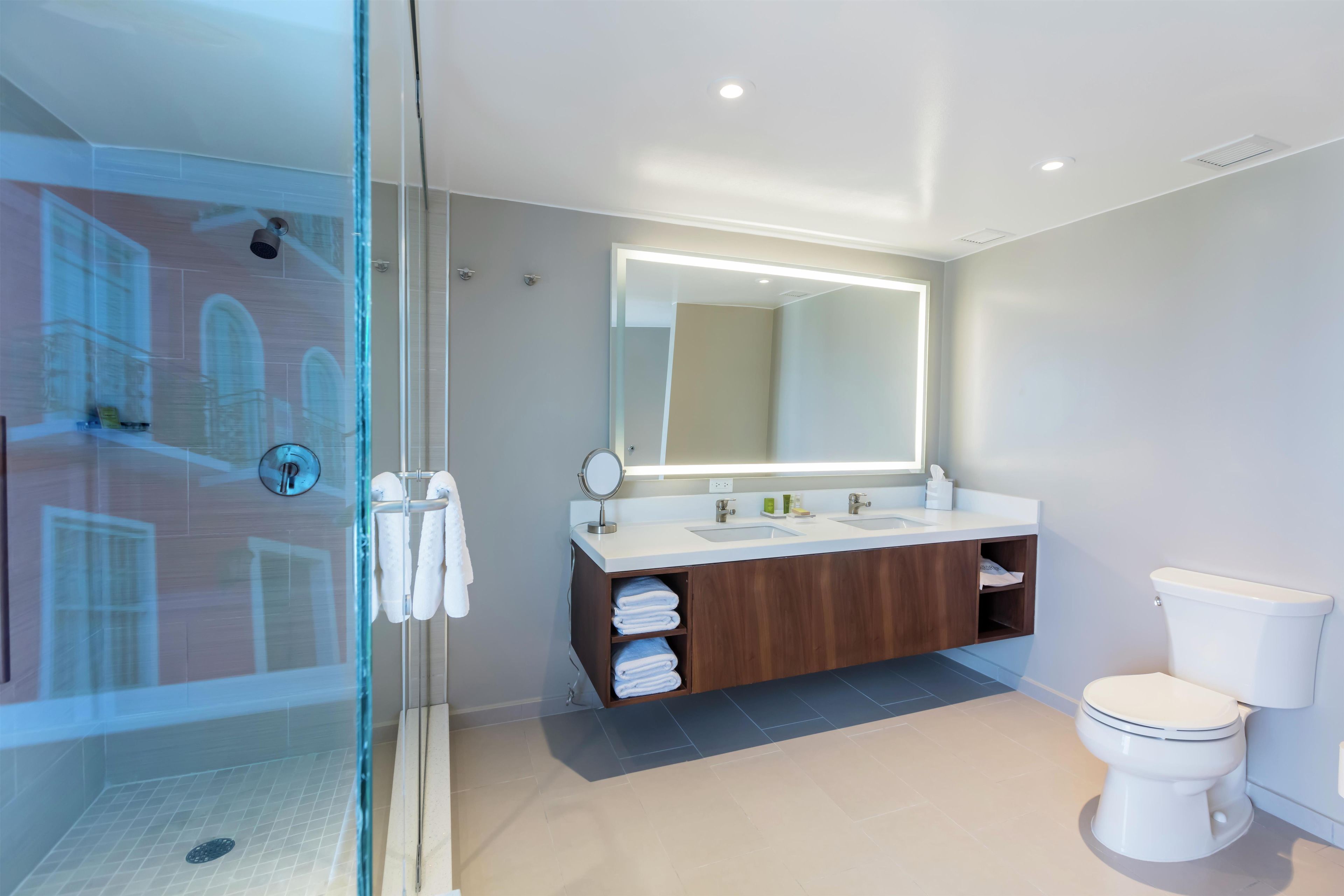 Un baño moderno con cabina de ducha de vidrio, un espejo grande y un mueble de tocador doble.