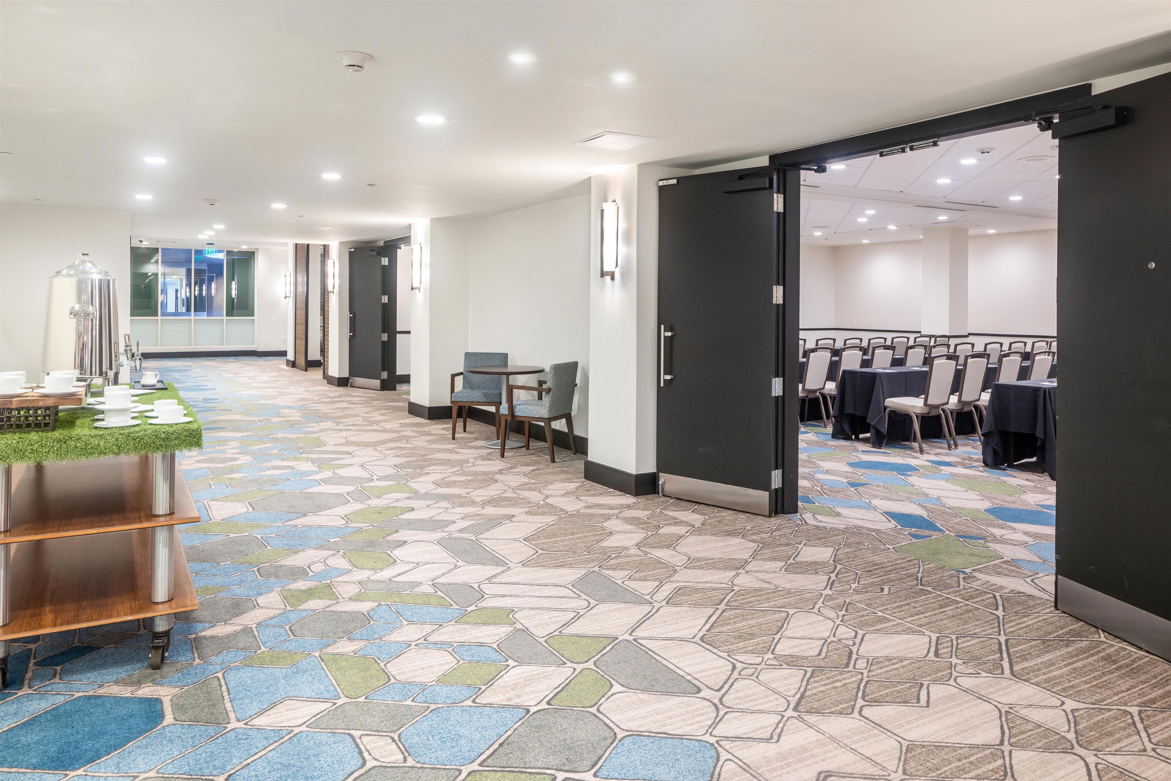 A hotel corridor with a patterned floor, a reception area with a coffee station, and a conference room with tables and chairs.