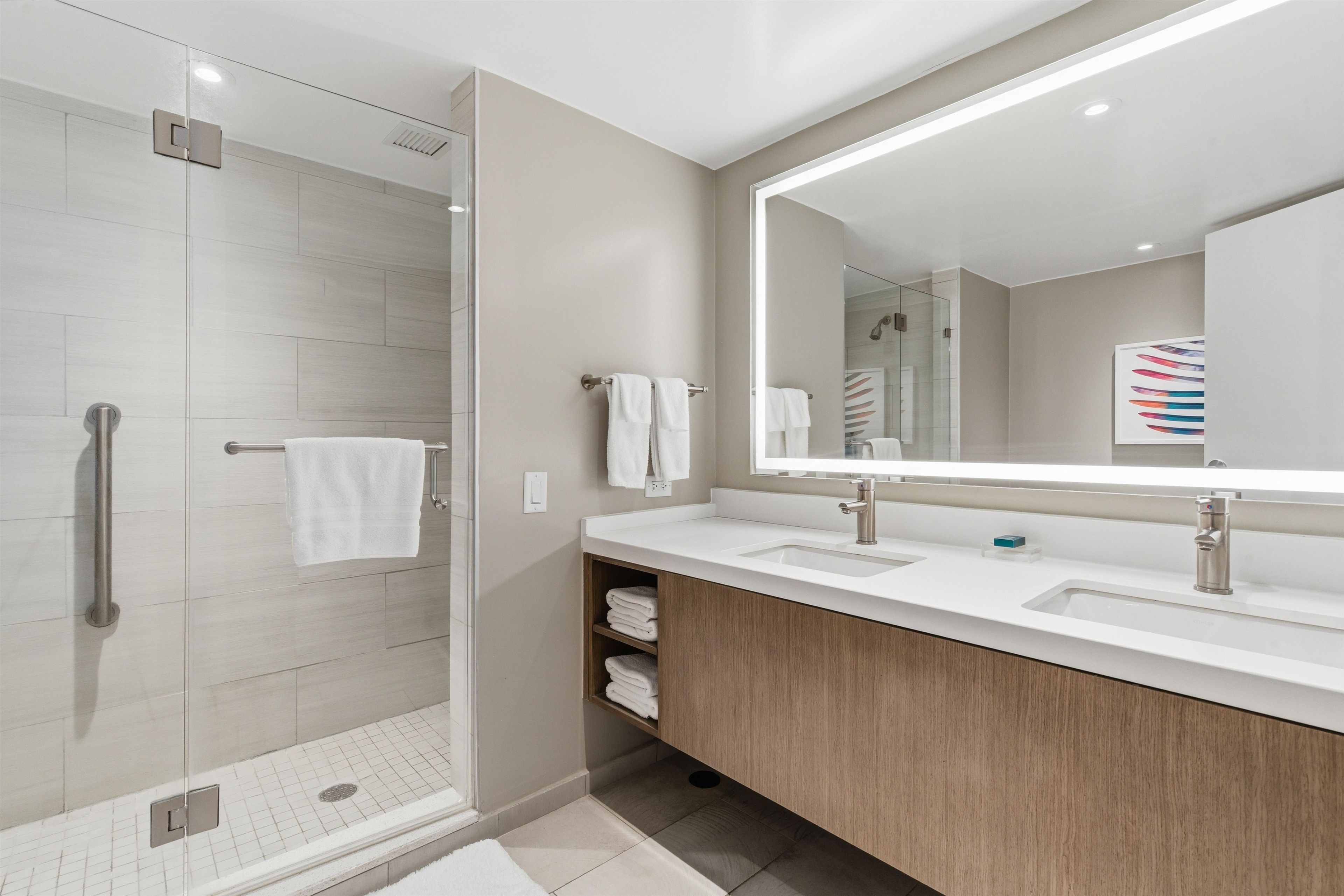 A modern bathroom with a glass shower enclosure, a large mirror, and a wooden vanity.