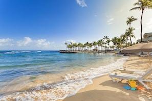 A beach with clear blue water, sandy shore, and palm trees. - Caribe Hilton (San Juan)