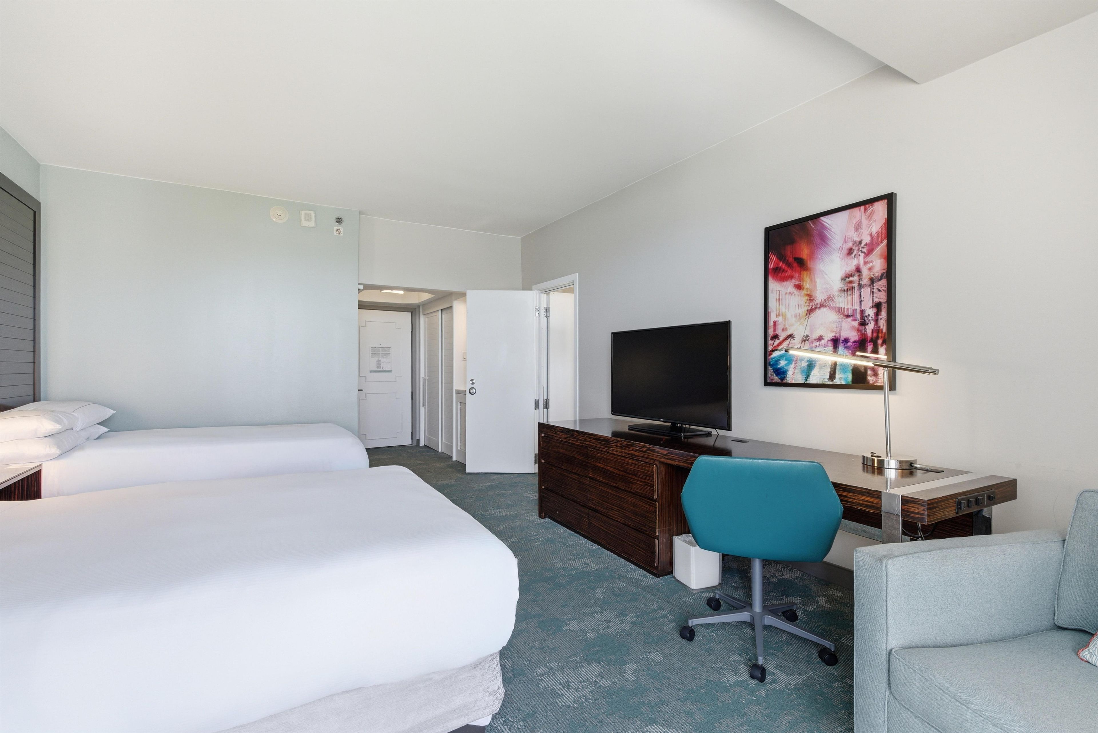 A hotel room with two beds, a desk with a computer, a TV, and a painting on the wall.